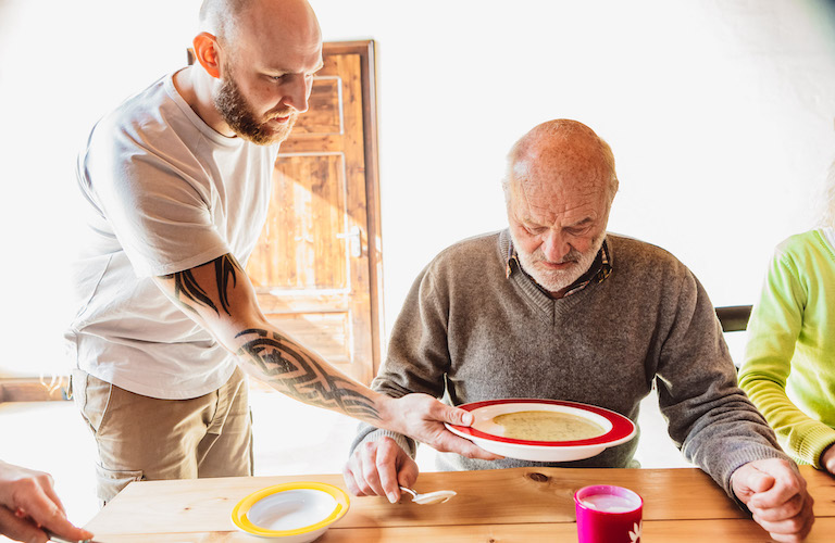 ORNAMIN- Teller mit Kipp-Trick Ein Pflege serviert einem Pflegebedürftigen eine Suppe