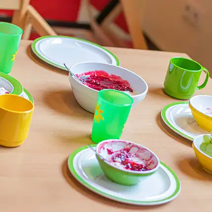 Buntes Kindergeschirr steht auf einem Esstisch in der Kita