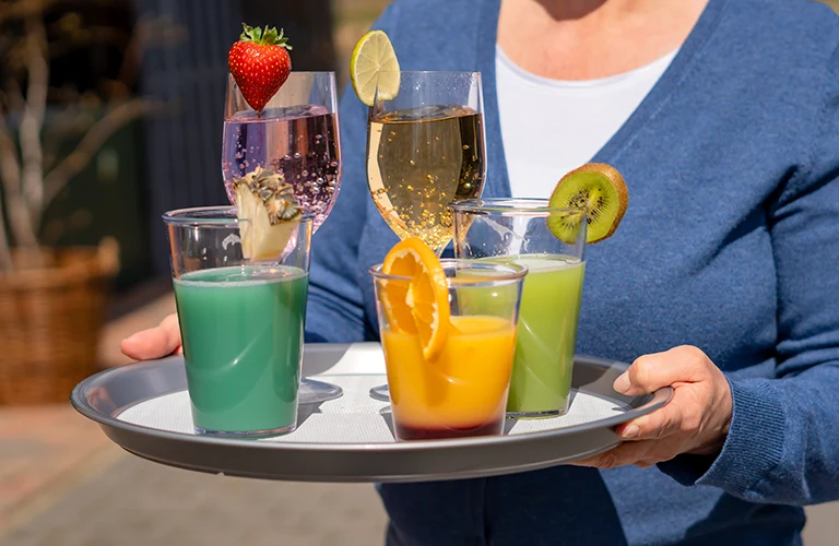 Eine Kellnerin serviert verschiedene Cocktails in Mehrwegbechern für den Genuss im Freien