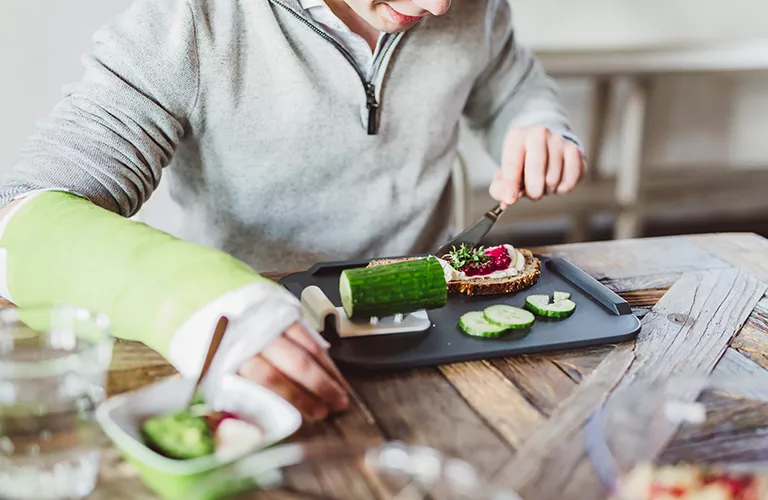 Ein junger Mann mit Gipsarm schneidet eine Gurke. A young man with a plaster arm cuts a cucumber.