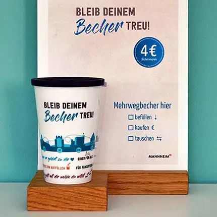 ORNAMIN-Coffee-to-go-Mehrwegbecher-im-Mehrwegsystem-in-Mannheim-neben-passendem-Werbeaufsteller