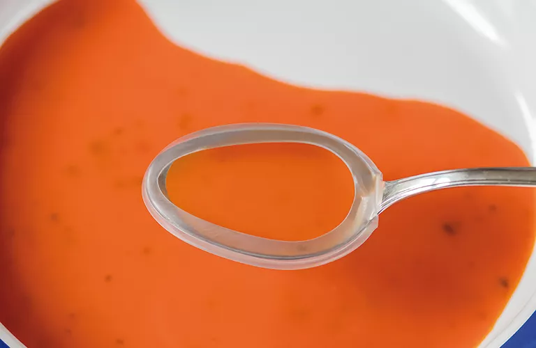 Ein Löffel mit Suppe mit Tremor-Löffelaufsatz. A spoon with soup with spoon guard.