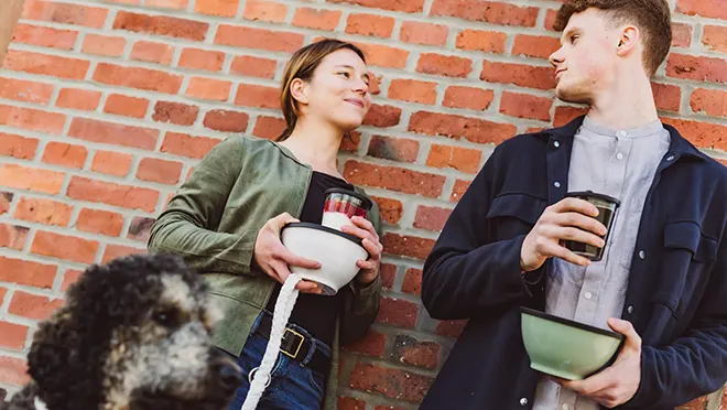 ORNAMIN-To-go-Mehrweggeschirr-für-Städte-und-Kommunen ORNAMIN-Zwei junge Menschen unterwegs in der Stadt mit ORNAMIN To go Mehrwegschale und Coffee To go Mehrwegbecher