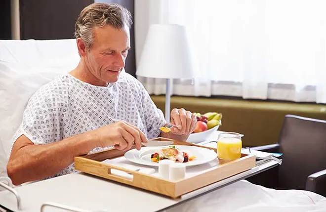 ORNAMIN-Pflege-Geschirr für die professionelle Pflege im Krankenhaus Mann im Krankenbett isst von einem Tablett mit professionellem Pflegegeschirr