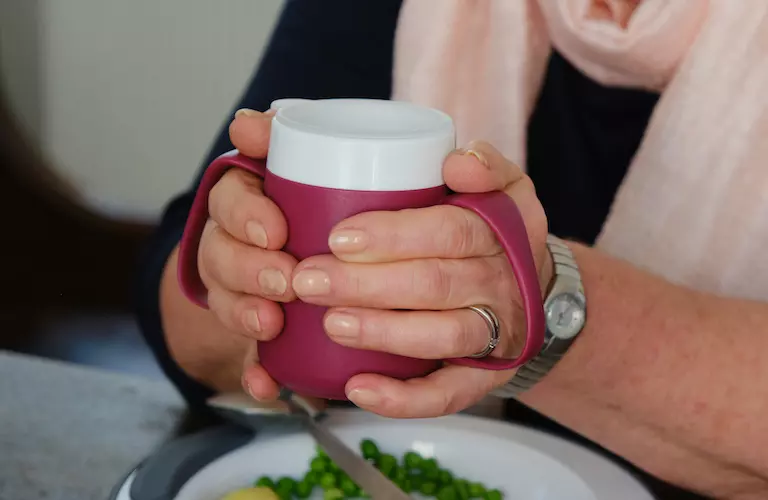 ORNAMIN-Becher mit Trink-Trick Zwei Hände halten einen Becher mit Trink-Trick. Two hands hold a cup with special drinking features.